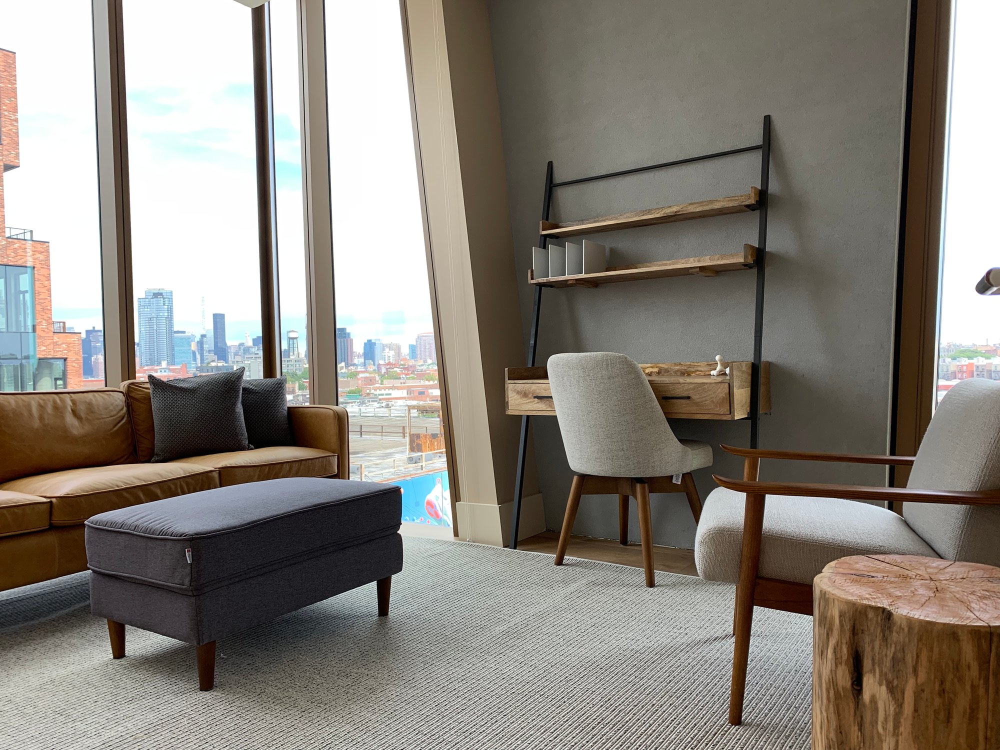 Modern therapy office with a leather sofa, wooden desk, and panoramic city views through floor-to-ceiling windows