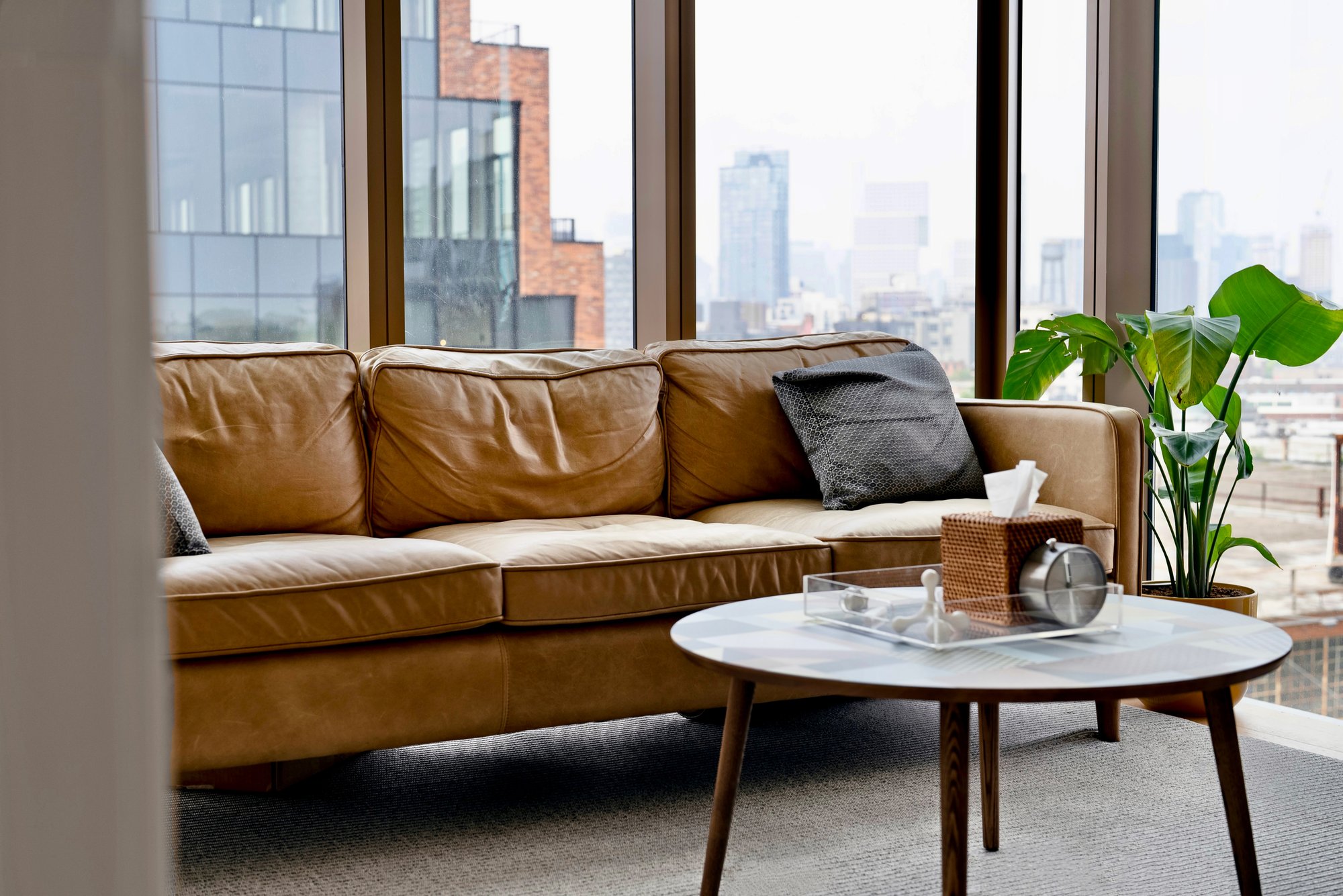 Modern therapy office with a leather couch, marble coffee table, and large windows overlooking the city