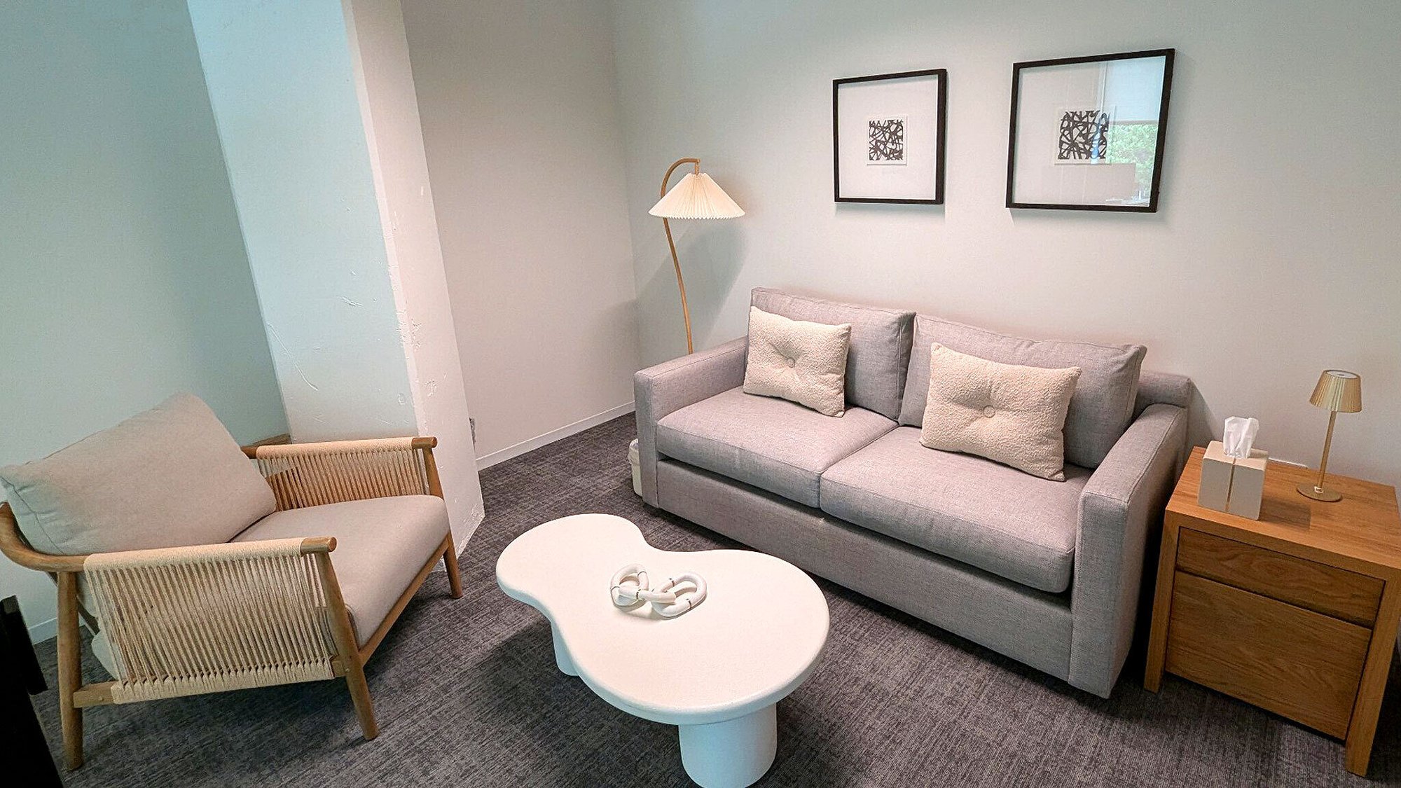 A cozy therapy office with warm lighting, a gray sofa, armchair, and round coffee table